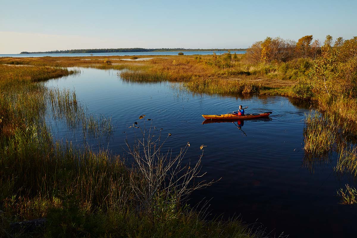 A kayaker floats on a peaceful creek at sunrise in early fall.