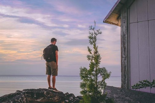 A man standing on a rock looking out at the lake.