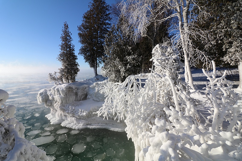 Edge of an iced over lake with snow covered trees