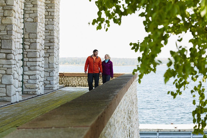 A couple walking near a stone facade with water in the background