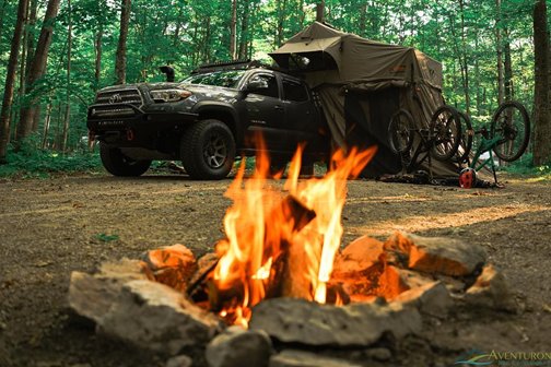 A campfire with a tent and mountain bikes in the background