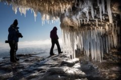 Two people walking just outside an ice-filled cave