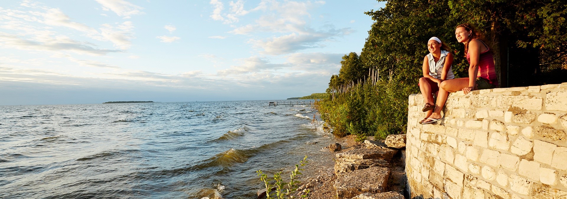 Two women sitting on a stone wall looking out at the lake.