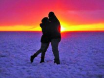A couple standing in the snow hugging at sunset.