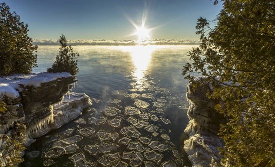 The sun rising over the lake beyond snowy bluffs.