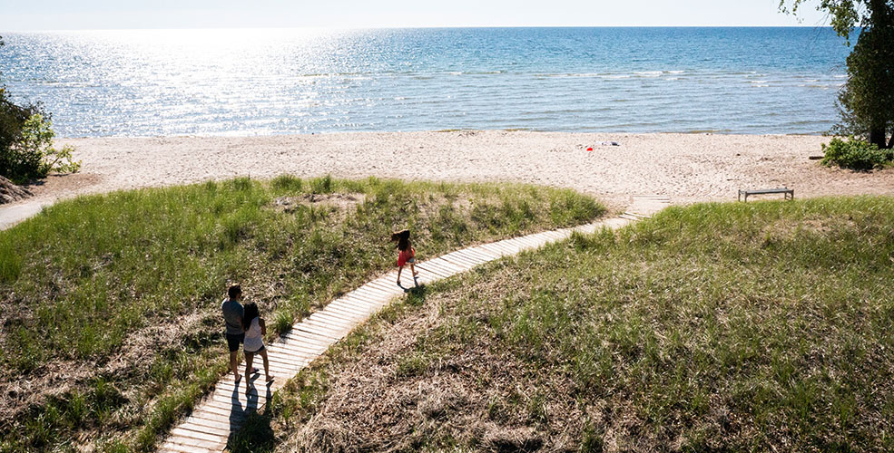 A family walking on a boardwalk down to the beach.