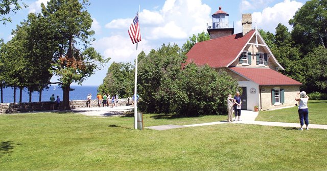 Woman taking a picture of two women standing in front of a lighthouse.