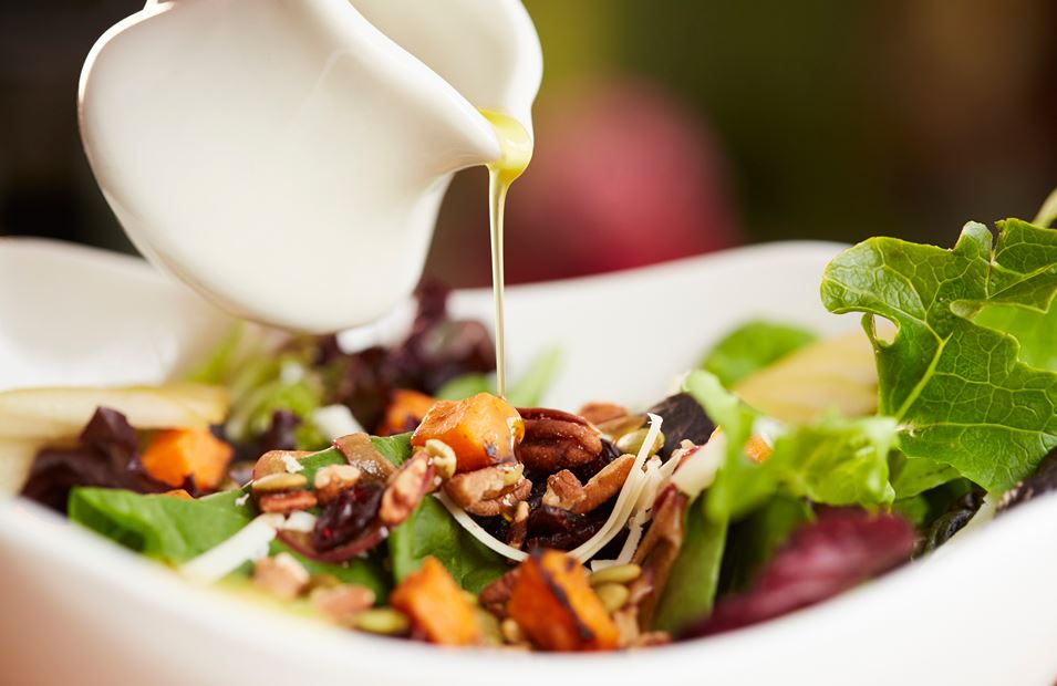 A salad with dressing being poured over it.