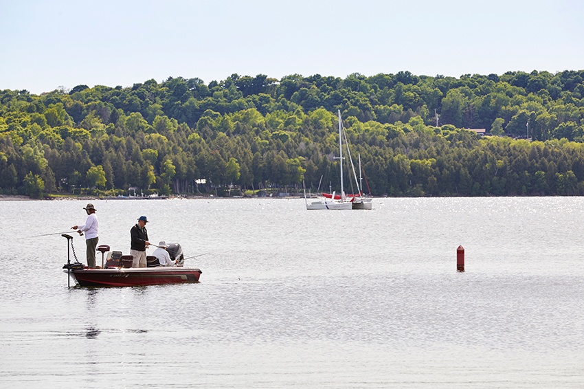 Men fish from a motor boat with a sailboat in the background