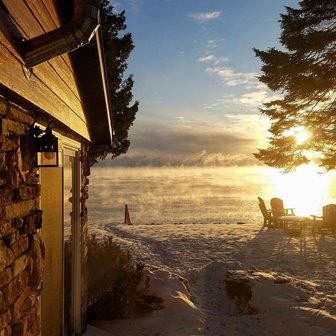 The sun rising over the lake near a log cabin.