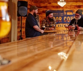 POV looking down a bar where a bartender and two customers are in conversation
