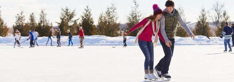 A couple ice skating with kids playing ice hockey in the background.