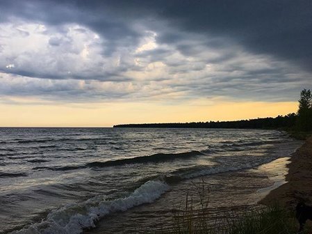 The sun setting over the lake on a cloudy day.