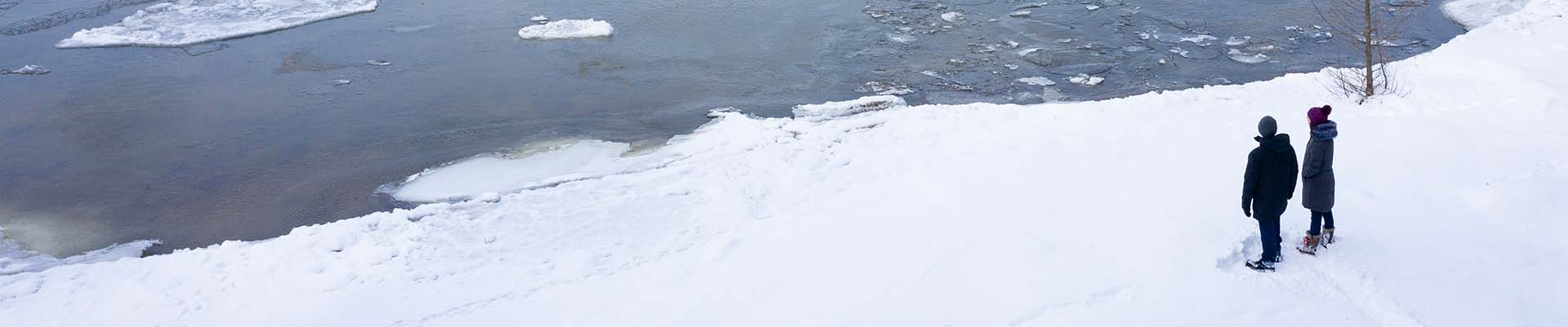 A couple standing on snow looking at the froze lake