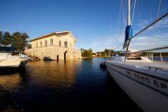 A sailboat in front of a stone boathouse