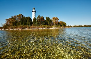 Point of view from shallow water offshore looking in on a lighthouse on an island.