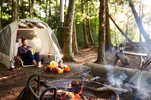 A woman reading in her tent at a campsite near a fire