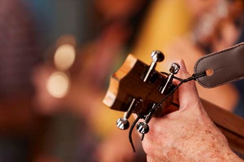 A man's hands play ukelele at an open mic night.