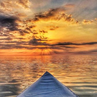 From the point of view looking out the front of a kayak toward the sunsetting